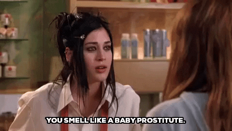 Janis Ian, a goth girl from Mean Girls, looks disturbed as she leans in to say to another woman, "You smell like a baby prostitute." She wears a white button down, red apron, and has long black hair