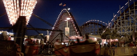 A night view of Santa Cruz Beach Boardwalk with people walking around and a roller coaster at an amusement park