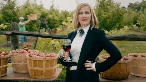 Moira Rose in an orchard, holding a glass of wine, toasting our credit card debt payoff