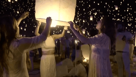 A group of people at a Quinceanera celebration, holding up a sky lantern and setting it alight.