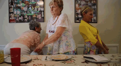 Three elderly women dancing in front of dinner table