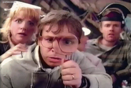 A GIF of a scene from Honey I Shrunk The Kids showing the adults gathered looking through a magnifying glass