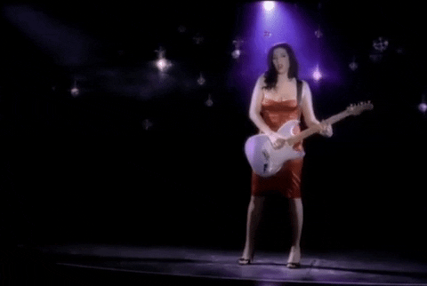 dark haired woman in a red dress playing an electric guitar under a spotlight