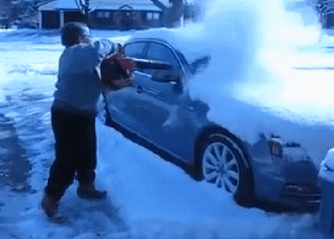 Une femme enlevant la neige sur sa voiture avec un souffleur à feuilles
