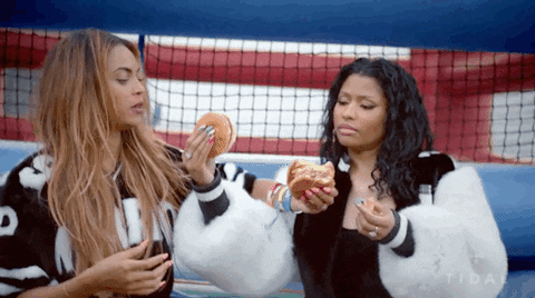 Singers Beyonce and Nicki Minaj eating a burger while entwined