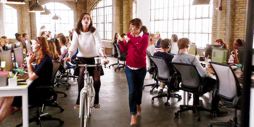 Woman biking in the office with other woman reading notes to her