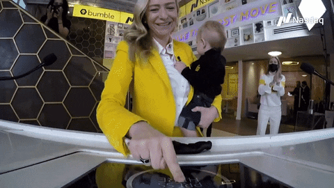 A gif of Bumble Founder and CEO Whitney Wolfe Herd ringing the bell at Bumble HQ for her company's IPO; in one arm, she is holding her infant son