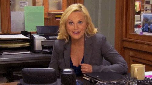 Blonde vrouw met een grijze blazer zit enthousiast aan haar bureau te knikken.