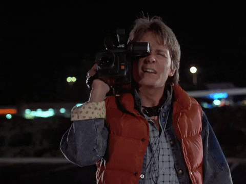 Martin McFly do filme De Volta para o Futuro segurando uma câmera muito grande para gravar o Professor Brown