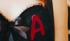 Emma Stone as Olive Penderghast in the movie 'Easy A'. In this GIF, she's blowing a kiss while wearing a red corset with the letter 'A' sewn on the front.