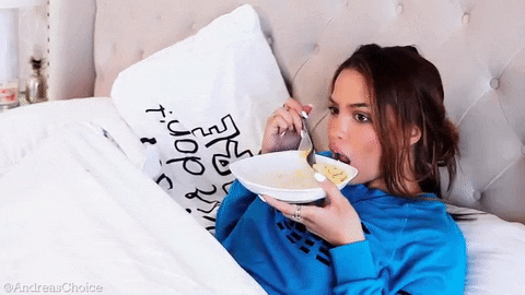 Woman in bed with a bowl of food and pushing food into her mouth with a spoon