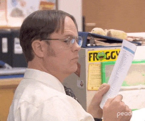 The Office: Dwight Schrute holds a sheet of paper and turns his eyes sideways, suspicious.