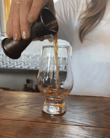 Woman pours whiskey into a glass.