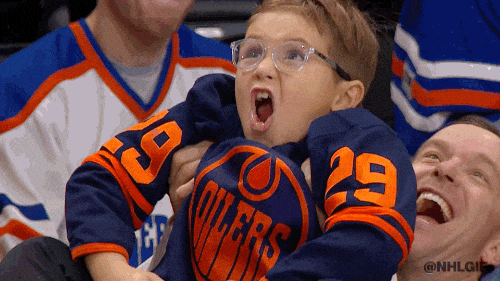 A little boy in a hockey jersey cheers and pumps his fists.
