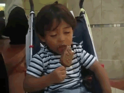 a little boy falling asleep while eating his ice cream on a stick