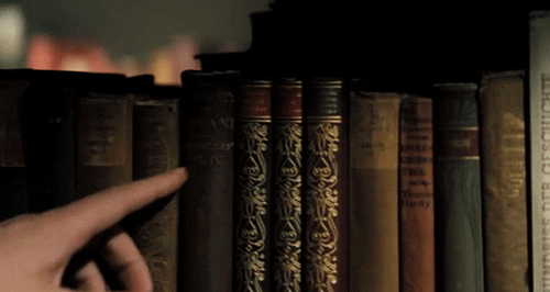 A person slides his or her finger across multiple old, embellished books.