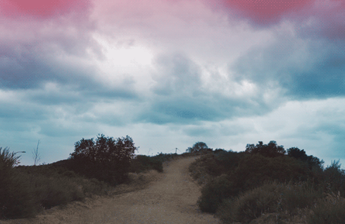 Generous, pink-and-blue clouds pass over a dusty trail