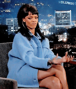 GIF of Rhianna wearing a large blue jacket making the money hand-signals.