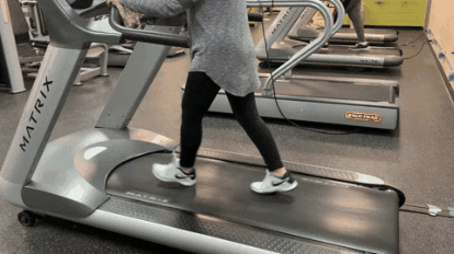 Person walking steadily on a gym treadmill, filmed from the side at belt level