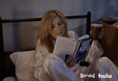 A gif of a woman getting cozy in bed with a coffee and a book