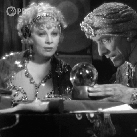 Footage from a black and white movie; two people in fancy costumes look into a crystal ball.