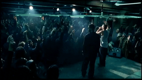 GIF of Eminem in the movie Eight Mile rapping in front of a crowd in a dark basement club with the crowd rapping with him