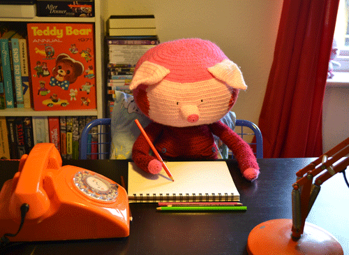 knitted pig character writing at its desk on a notepad in a bedroom