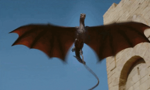 A small dragon, Drogon from Game of Thrones, flaps its wings to stay in the air as it breathes fire. 