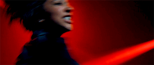GIF from the TV show We Are Lady Parts. On a stage lit with red lights, a woman plays electric guitar while singing and headbanging.
