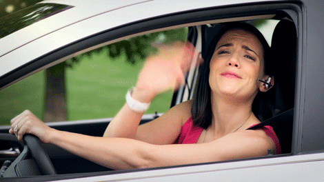 A woman waves, blows a kiss to the camera, and then drives away.