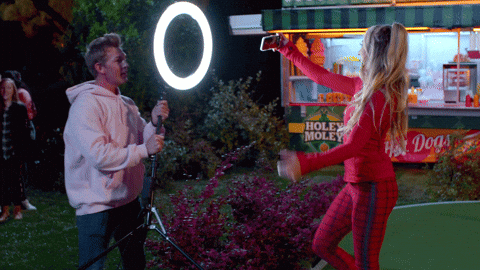 Gif of an influencer taking a selfie while a guy holds a ring light