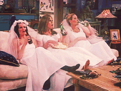 Gif of Monica, Rachel, and Phoebe from Friends watching tv in wedding dresses, drinking beer and eating popcorn.