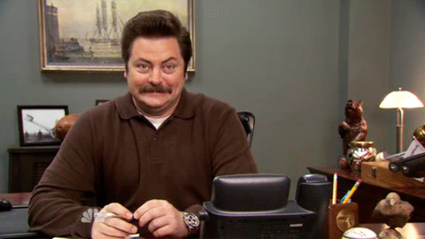 Parks and Recreation: Ron Swanson sits at his desk and stares at the camera, unimpressed