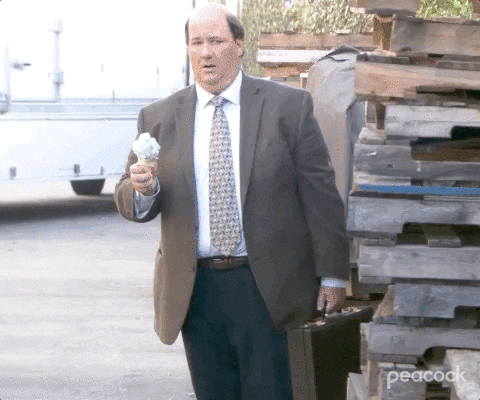 Gif of a man on wearing a suit, holding an icecream cone, looking at the camera as the ice-cream falls out of the cone