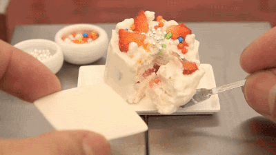 Person cuts and serves a miniature sized cake with strawberries and sprinkles.