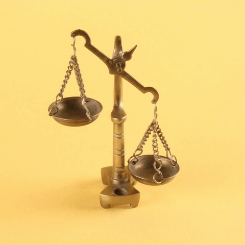Miniature scales of justice being balanced by a person's finger