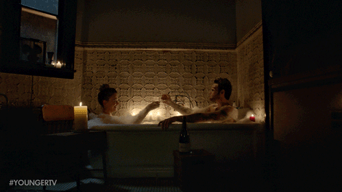 Couple enjoying a bubble bath with candles lit on the side