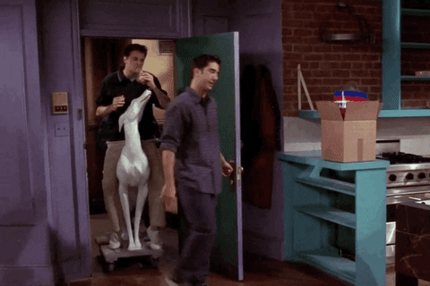 Animated Gif from the series Friends. The roommates Chandler and Joey arrive in the apartment on a white plastic dogs on wheels.