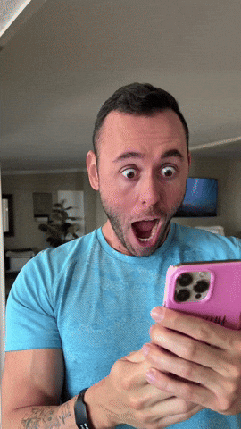 Man in a blue t-shirt covering his eyes with one hand while holding a pink phone in the other