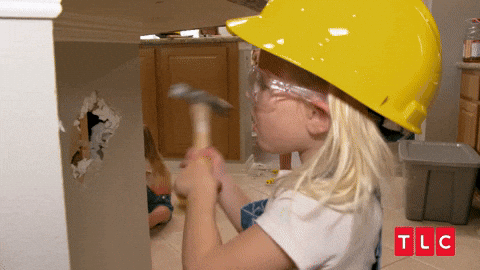 Gif of a small girl wearing a hard hat and safety goggles, hammering a wall