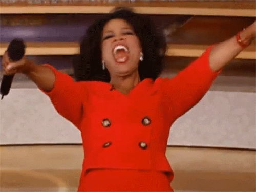 Oprah com um microfone gritando e apontando para a platéia