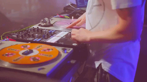 DJ working two turntables, one spinning an orange vinyl record